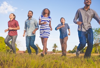 people running on grassfield under blue skies at daytime